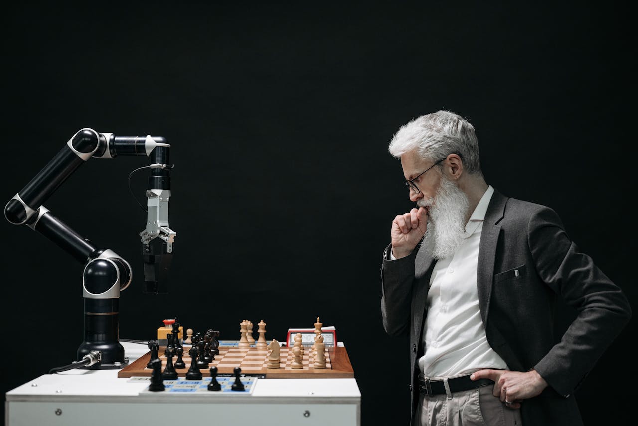 gallery-01 An elderly scientist contemplates a chess move against a robotic arm on a chessboard.